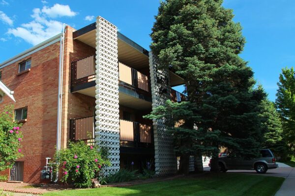 Exterior of 70 Clarkson apartments with bushes, grass, and a large tree.