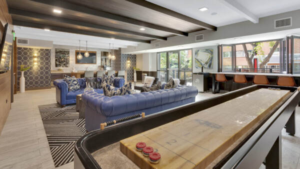 Clubroom with shuffleboard table, plush leather couches, modern furniture, and large windows.