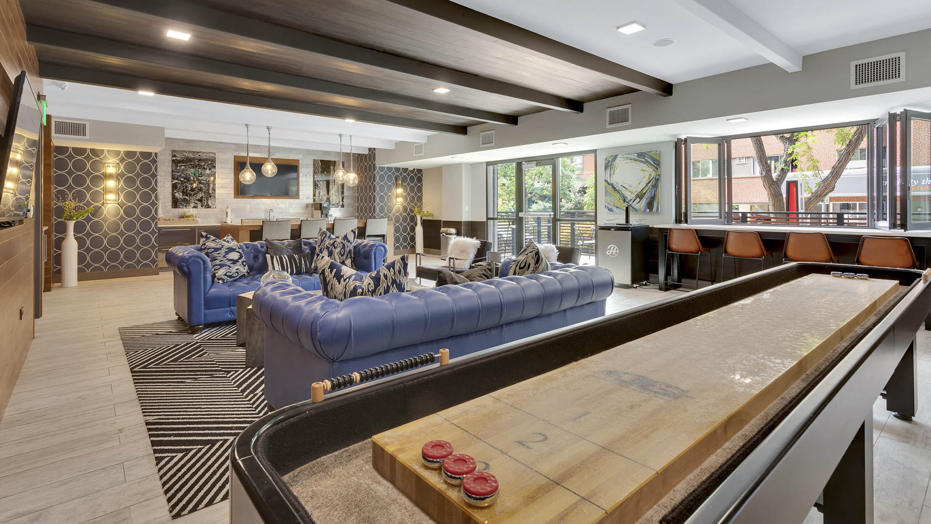 Clubroom with shuffleboard table, plush leather couches, modern furniture, and large windows.