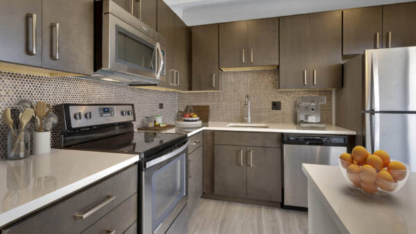 Kitchen with wood floor and cabinets, light counters, stainless steel appliances, and bowl of oranges.
