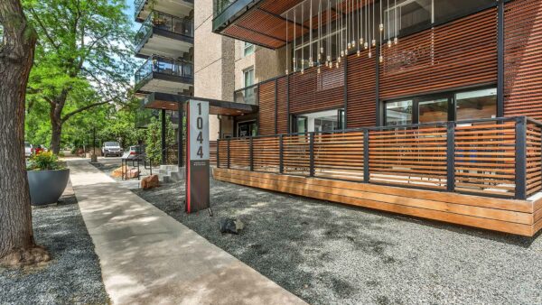 1044 Downing apartment entrance with rocky landscaping, mature trees, and patio area with light fixtures.