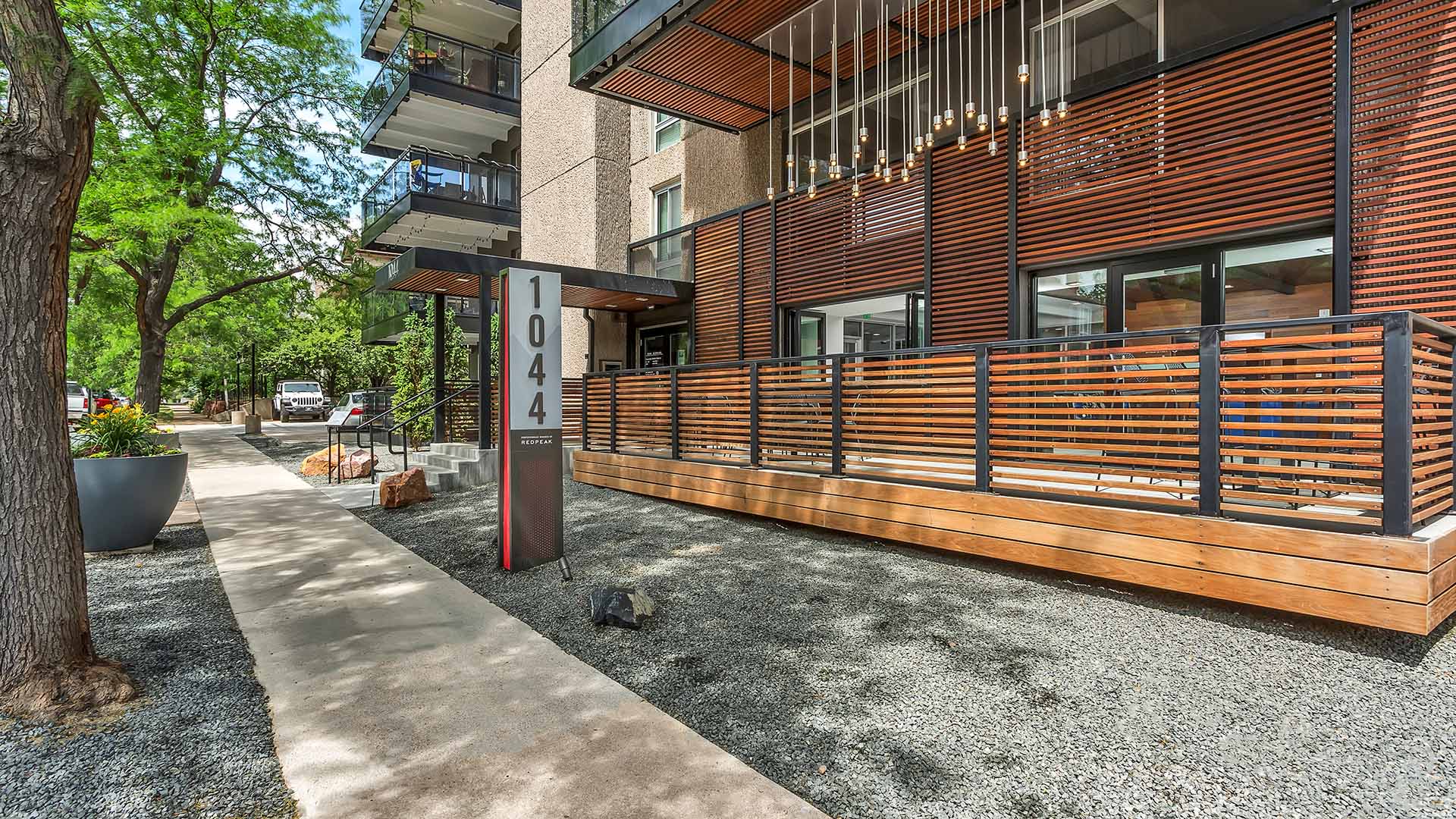 1044 Downing apartment entrance with rocky landscaping, mature trees, and patio area with light fixtures.