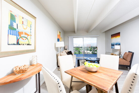 Living room with wood floor, rug, plush seating, dining table, artwork, and sliding door to balcony.