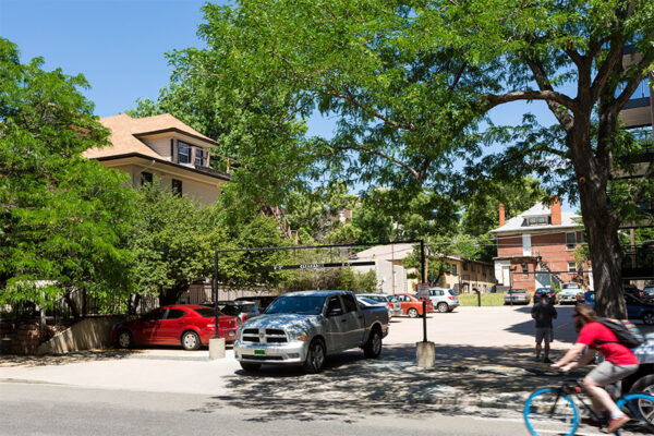 1044 Downing parking lot with parked cars and tall trees.