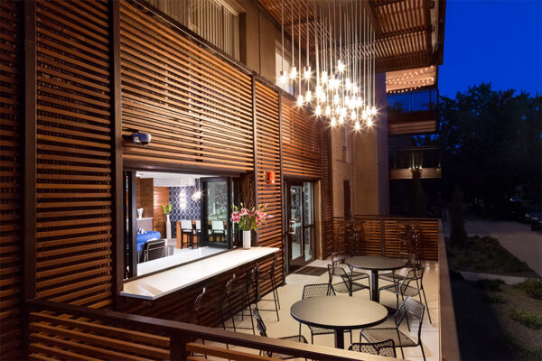 Indoor outdoor lounge with sliding window, patio seating, and bright chandelier.