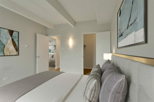 Bedroom with large bed with plush headboard, framed artwork, and doors to closet and hallway.