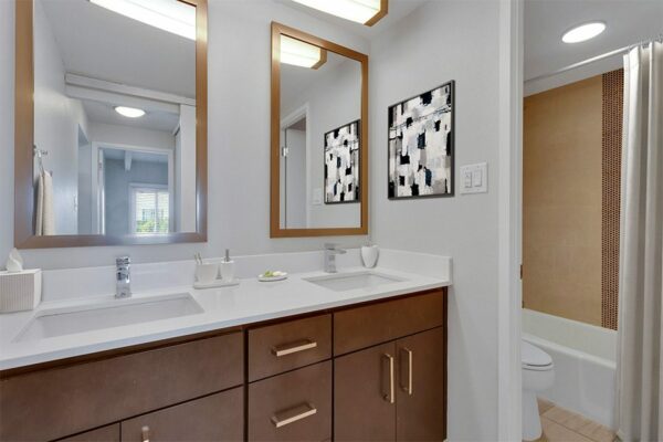 Bathroom with wood cabinets, light counter, dual sinks with framed mirrors, and artwork.