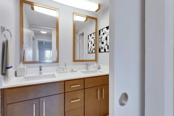 Bathroom with wood cabinets, light counter, dual sinks with framed mirrors, and large light fixture.