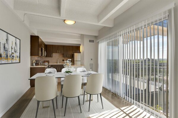 Dining room with modern table and chairs next to large bright window with blinds.