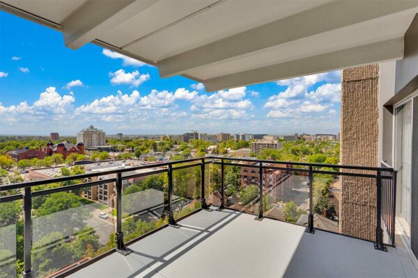 Balcony with metal and glass railing overlooking Denver under cloudy skies.
