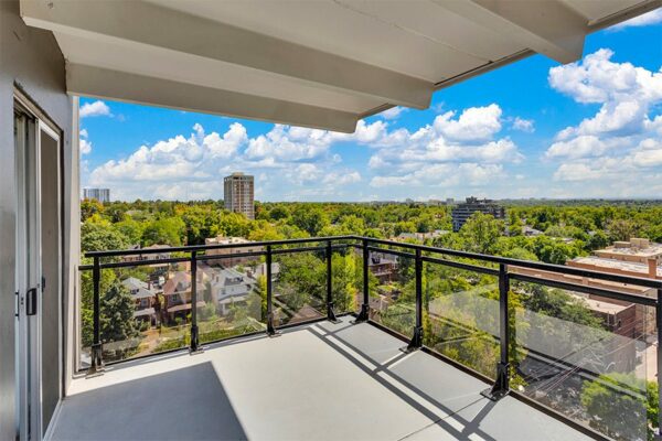 Balcony with metal and glass railing overlooking Denver under cloudy skies.