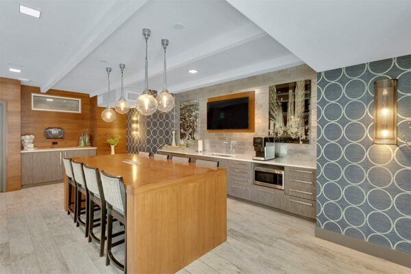 Community kitchen with wood floor, large dining table, geometric wallpaper, and wall mounted TV.