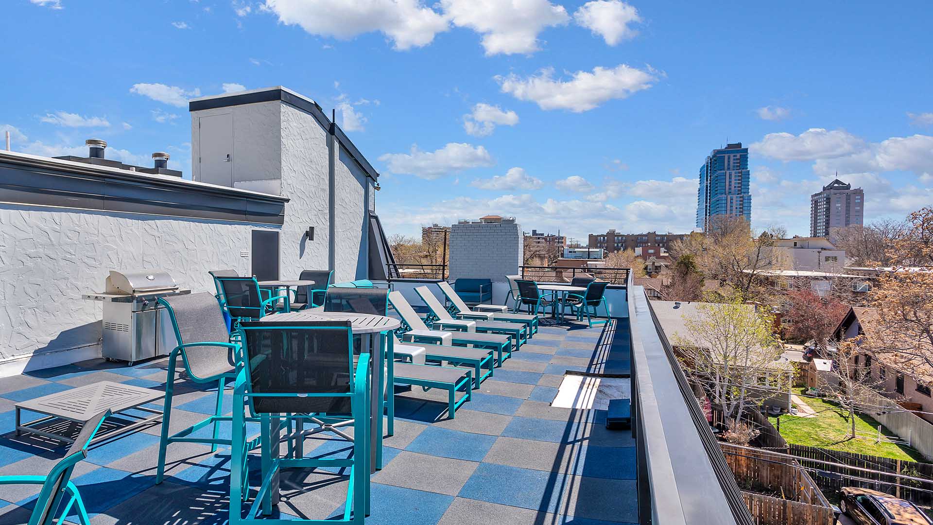 Rooftop patio with outdoor furniture, BBQ grill, and metal railing overlooking Denver.