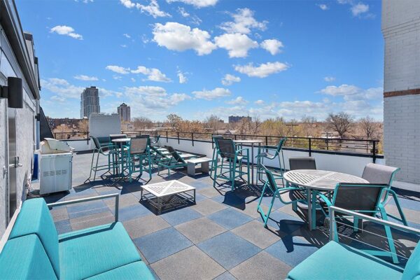 Rooftop patio with lounge chairs, tables, and BBQ grill overlooking Denver.