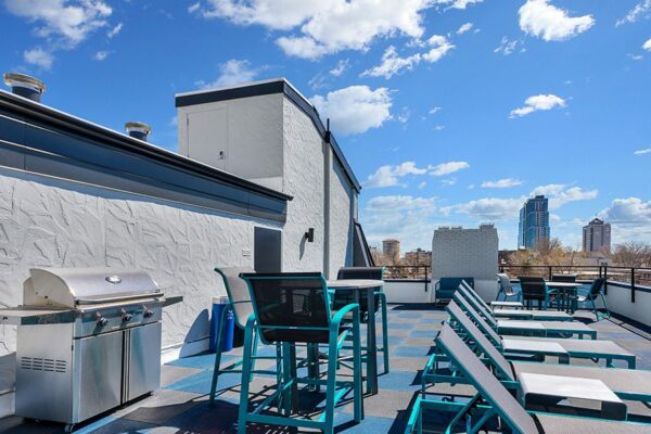 Rooftop patio with lounge chairs, tables, and BBQ grill overlooking Denver.