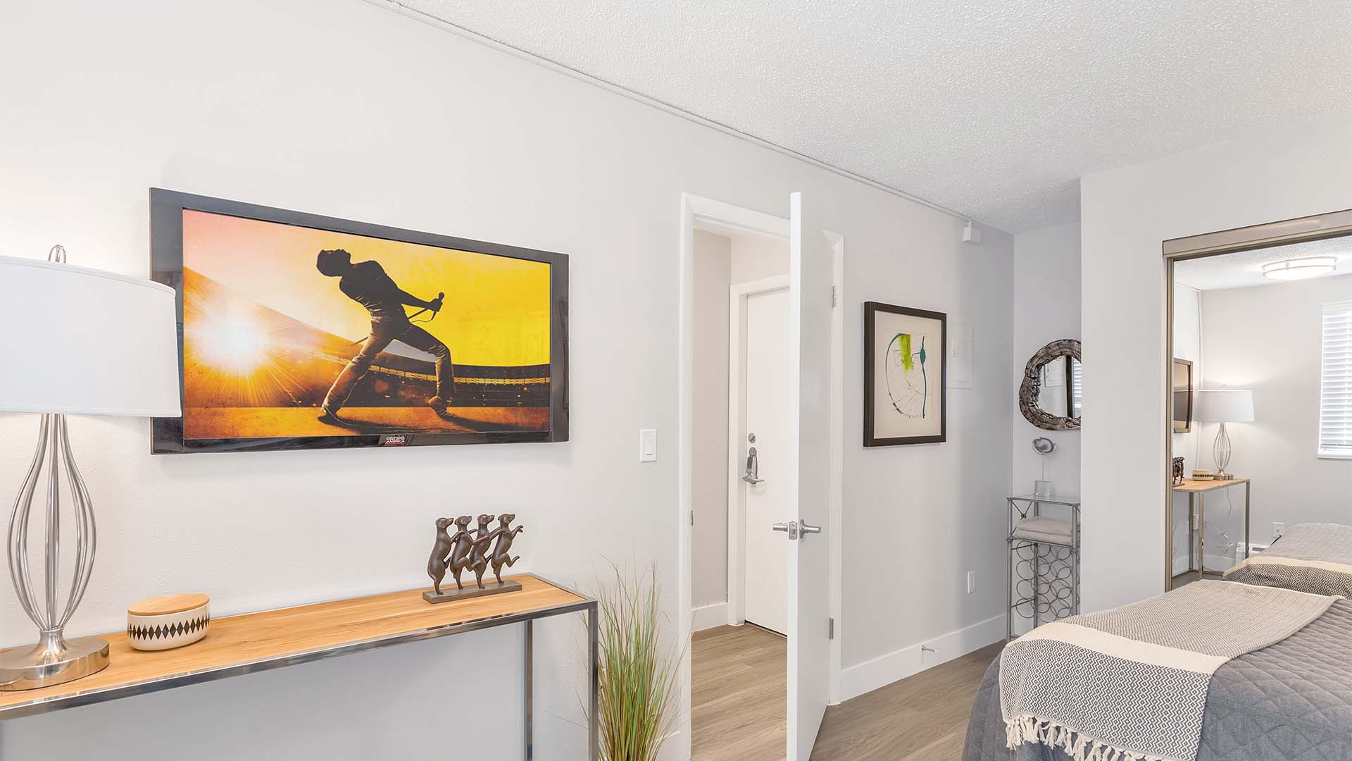 Studio apartment with modern furniture, plush bed, framed artwork, and large mirror closet door.