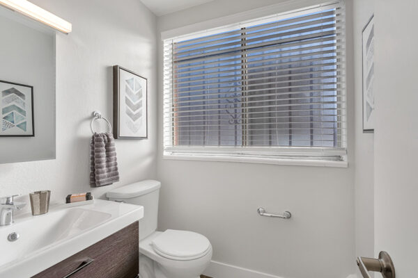 Bathroom with wood cabinets, white counter, large mirror, and window with blinds.