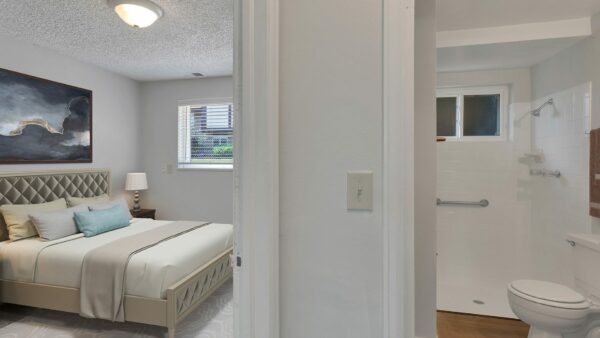 Bedroom with rug, bed with plush headboard, artwork, bathroom and window.