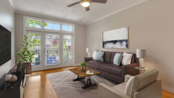 Living room with wood floor, plush furniture, wall mounted TV, and door to balcony.