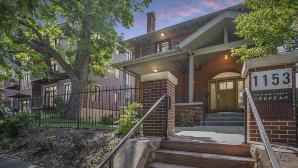 1153 Ogden apartments with classic brick construction, iron fence, and lush landscaping with mature trees.