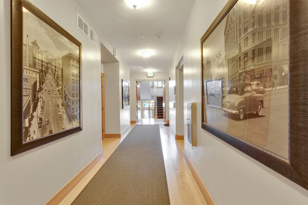 Hallway with wood floor, carpet runner, and vintage framed photographs.