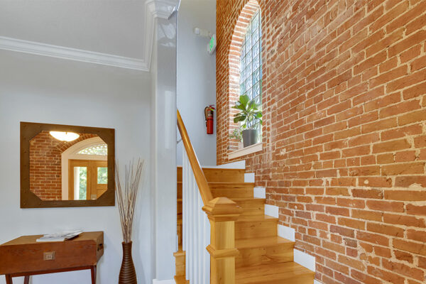 Stairway with wood treads, brick accent wall, and large window with potted plant.