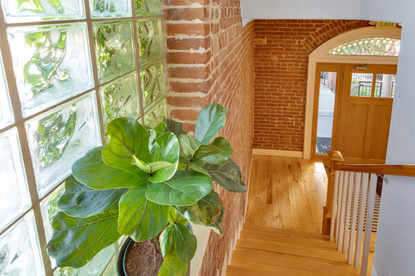 Stairway with wood treads, brick accent wall, and large window with potted plant.