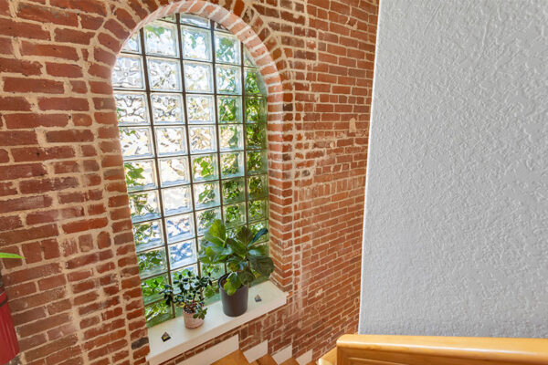 Stairway with wood brick accent wall and large window with potted plant.