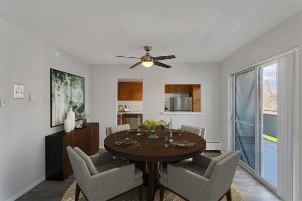 Dining area with round table, plush chairs, artwork, and large balcony door.