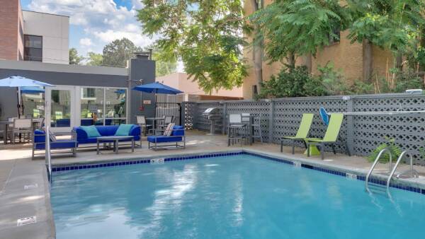 Pool area with patio, outdoor lounge chairs, sofa, and tables with umbrellas.