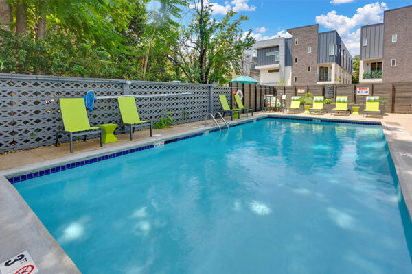 1190 Birch pool area with bright lounge chairs shaded by tall trees.