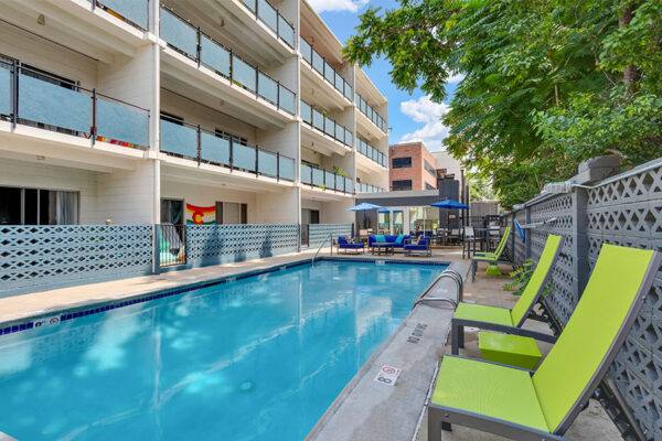 1190 Birch pool area with clean blue water, lounge chairs, and tables with umbrellas overlooked by apartment balconies.