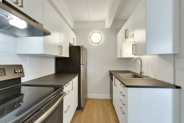 Kitchen with wood floor, white cabinets, dark counters, and stainless steel appliances.