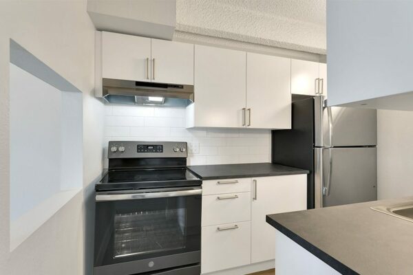 Kitchen with white cabinets, dark counters, stainless steel appliances, and opening to dining room.