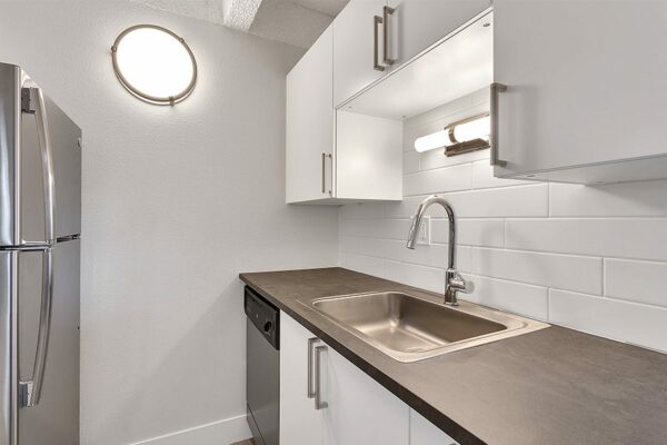 Kitchen with white cabinets, dark counters, stainless steel appliances, and tiled backsplash.