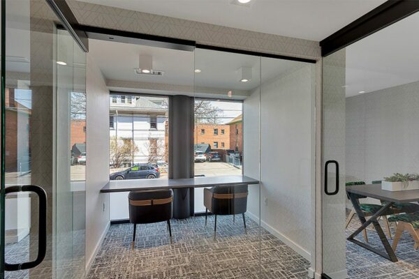 Business center with glass wall, built in desk, and modern office chairs.