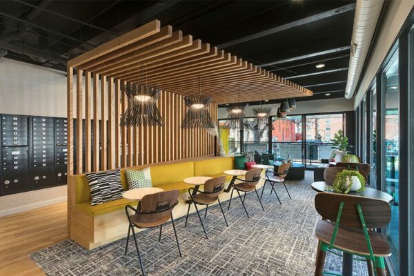 Lounge with carpet, plush booths with tables, decorative lighting fixtures, and wood slats.