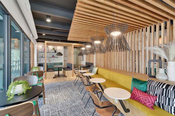 Lounge with carpet, plush booths with tables, decorative lighting fixtures, and wood slats.