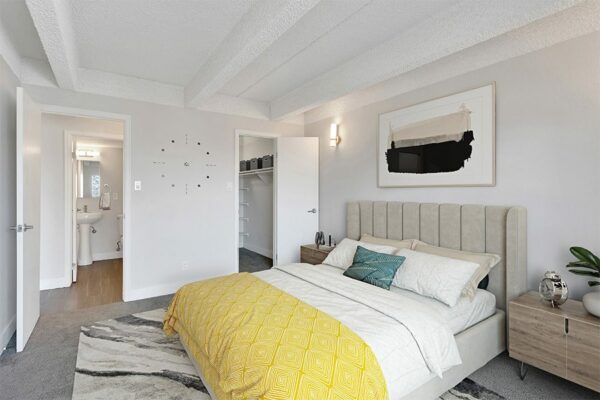 Bedroom with rug, bed with plush headboard, modern wood furniture, artwork, and door to bathroom and closet.