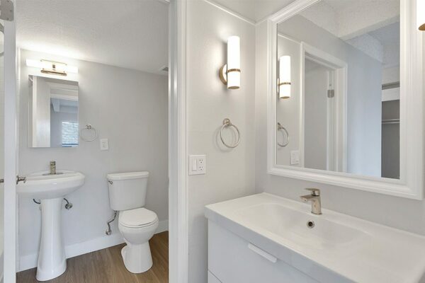 Bathroom with white cabinets and sink, framed mirror, and wood floors.