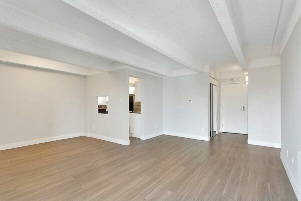 Living area with wood floor, grey walls, white trim, and doors to kitchen and hallway.
