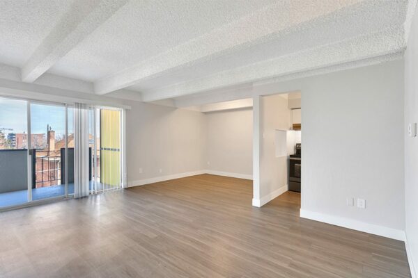 Living area with wood floor, grey walls, white trim, and doors to kitchen and balcony.