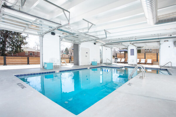 Indoor pool area with lounge chairs and garage doors to outdoor patio area.