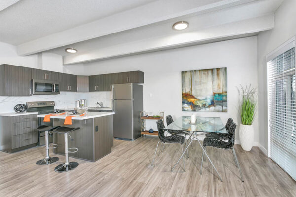 Kitchen and dining area with wood floor and cabinets, island with stools, and glass dining table with modern chairs.