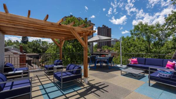 Rooftop patio with plush outdoor furniture, wood pergola, and metal railing overlooking Denver.