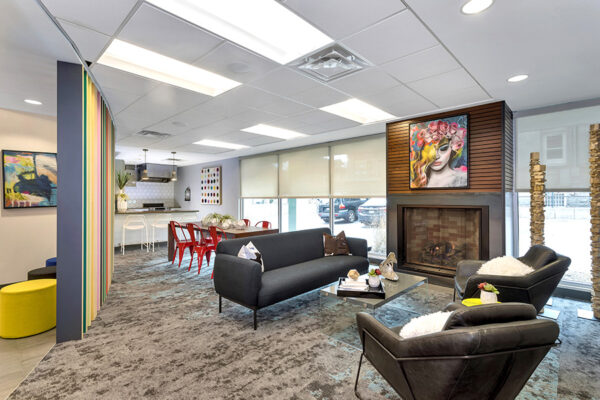 Lounge with carpet, comfortable modern furniture, built in fireplace, and large colorful painting.