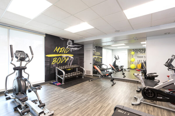 Fitness center with wood floor, mirror wall, dumbbell racks, and cardio machines.