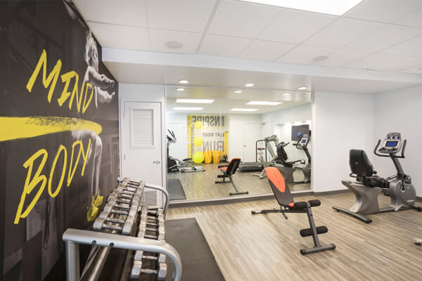 Fitness center with wood floor, dumbbell rack, and cardio machines.