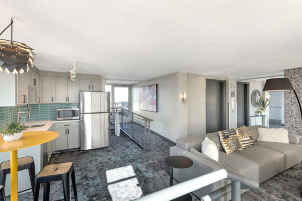 Lounge with kitchen, modern plush couch, tall bar table with stools, and eclectic decor.