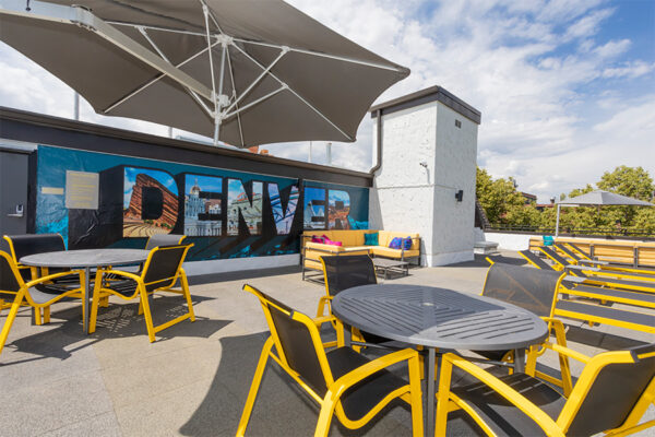 Rooftop patio with dining tables, large umbrella, and Denver mural.